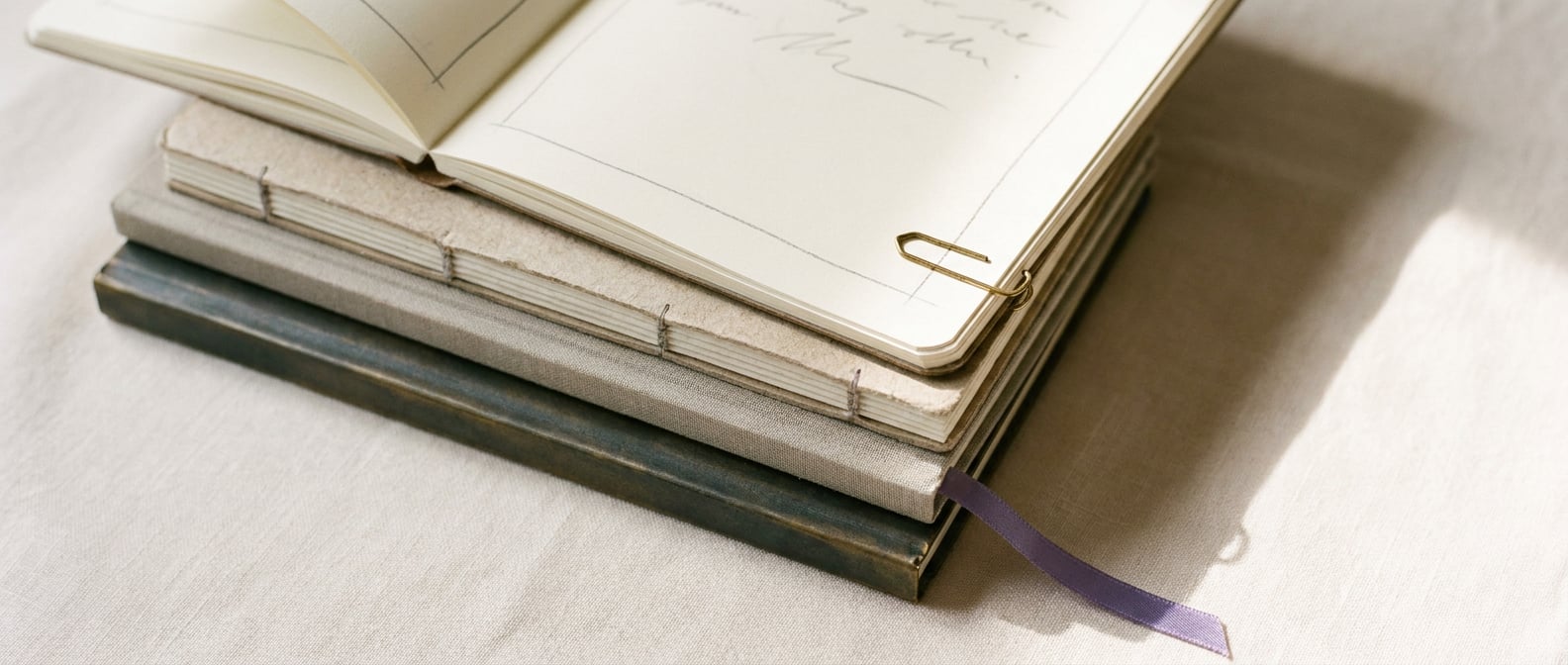 Aufgeschlagenes Notizbuch mit handschriftlichen Bleistift-Anmerkungen am Rand, lavendelfarbenes Lesebändchen, warmes Tageslicht.